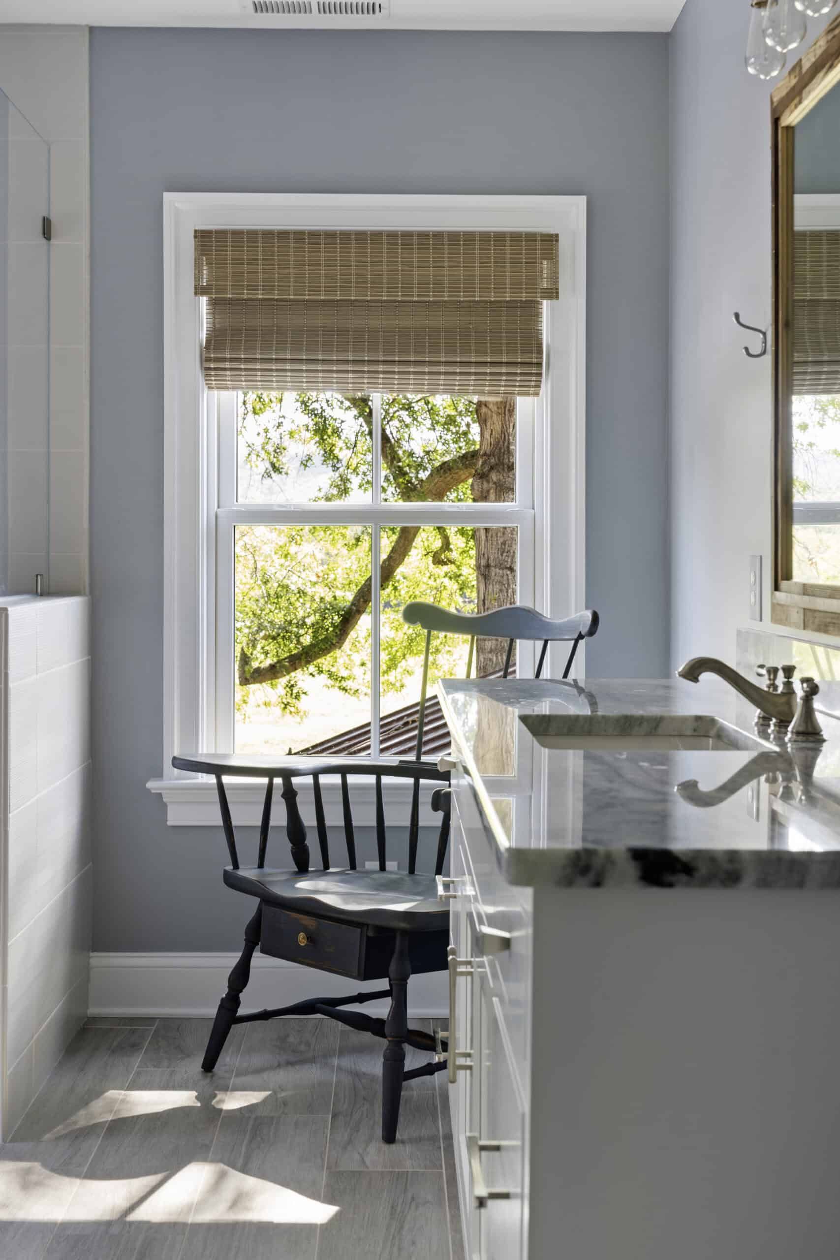 vanity with marble top in front of a window and antique wood chair