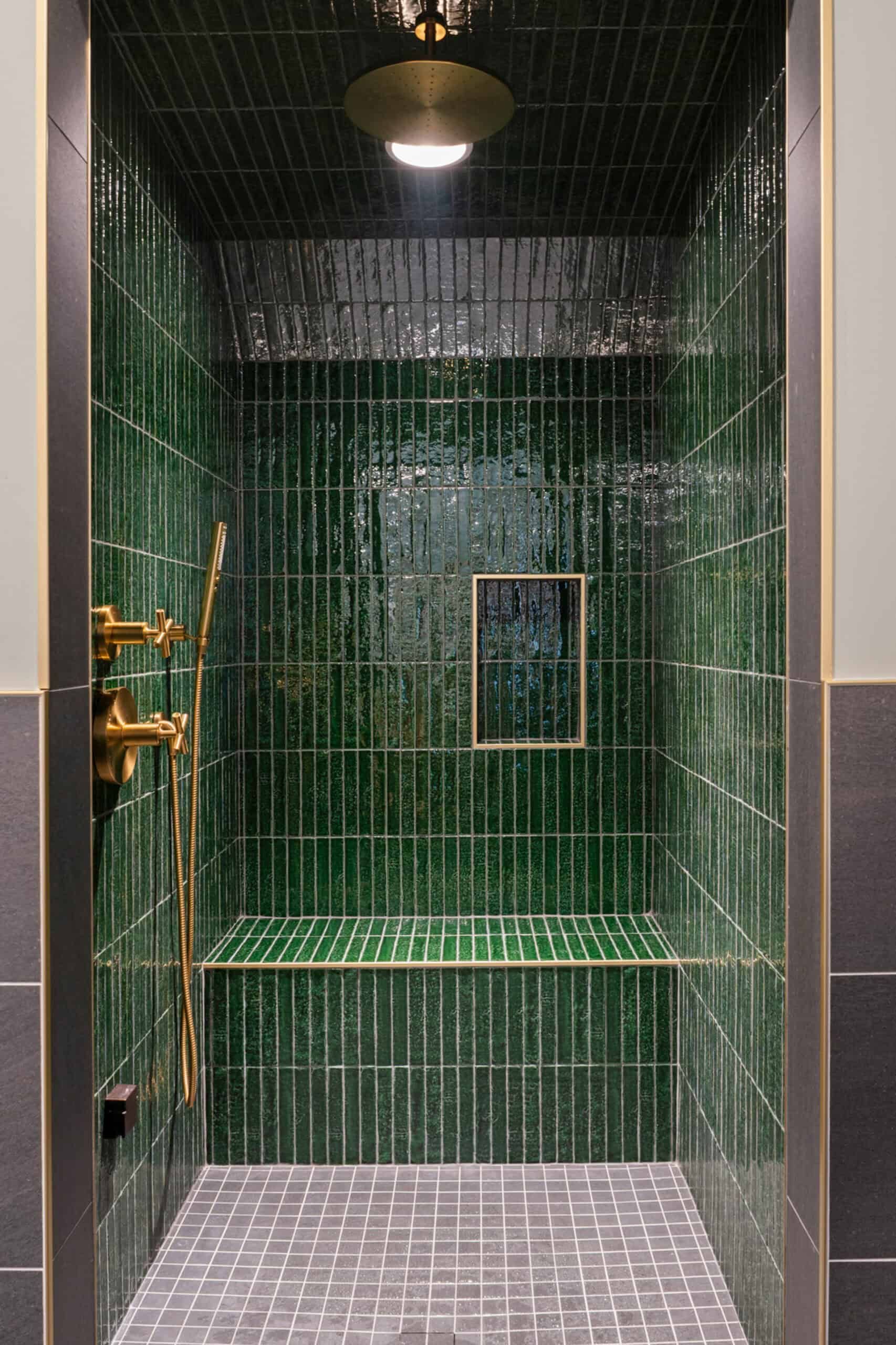 full view of walk-in shower with integrated bench. The walls and ceiling are covered with emerald tiles, the faucet and controls are brass
