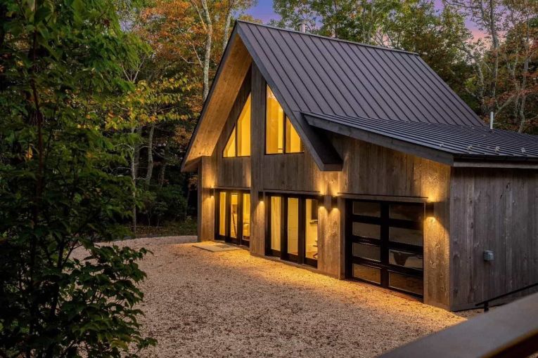 exterior of a natural wood finished cabin with a modern design at dusk with its lights on