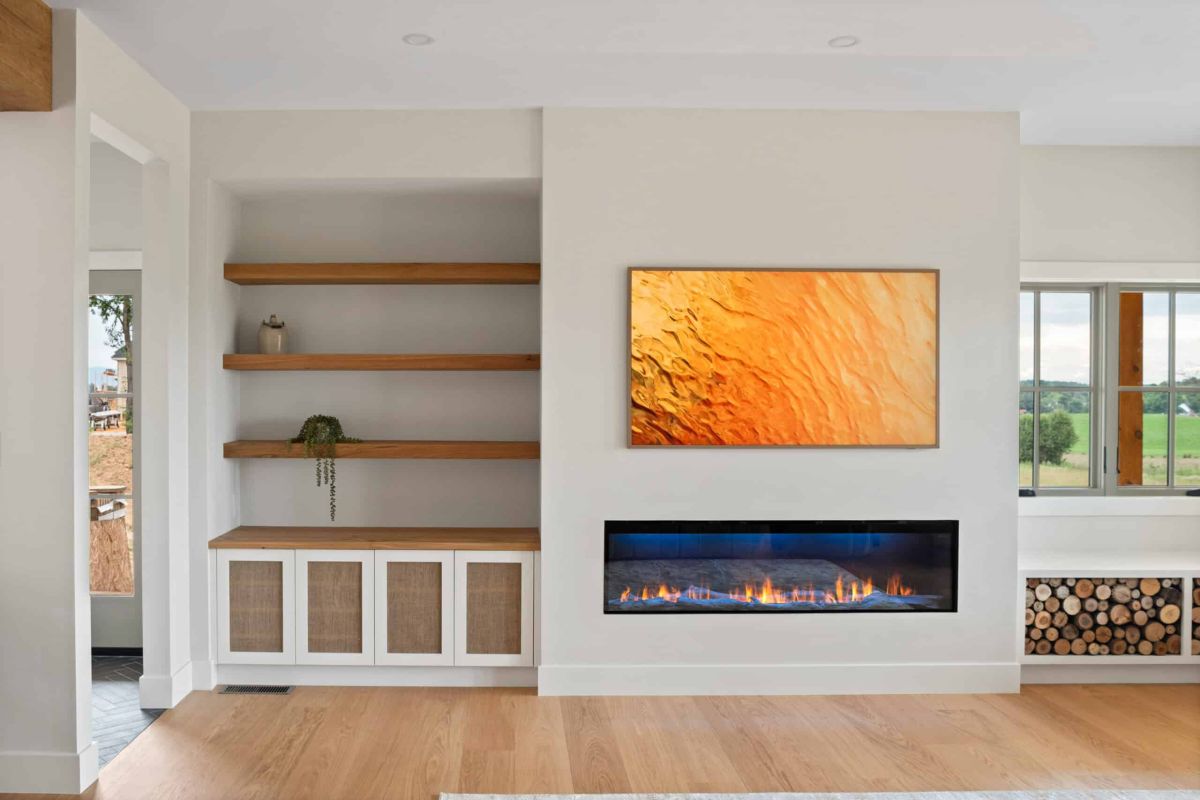 brightly lit family room, with a flatscreen tv mounted on the wall above a fireplace. some shelfs are on the left and wood logs on the right