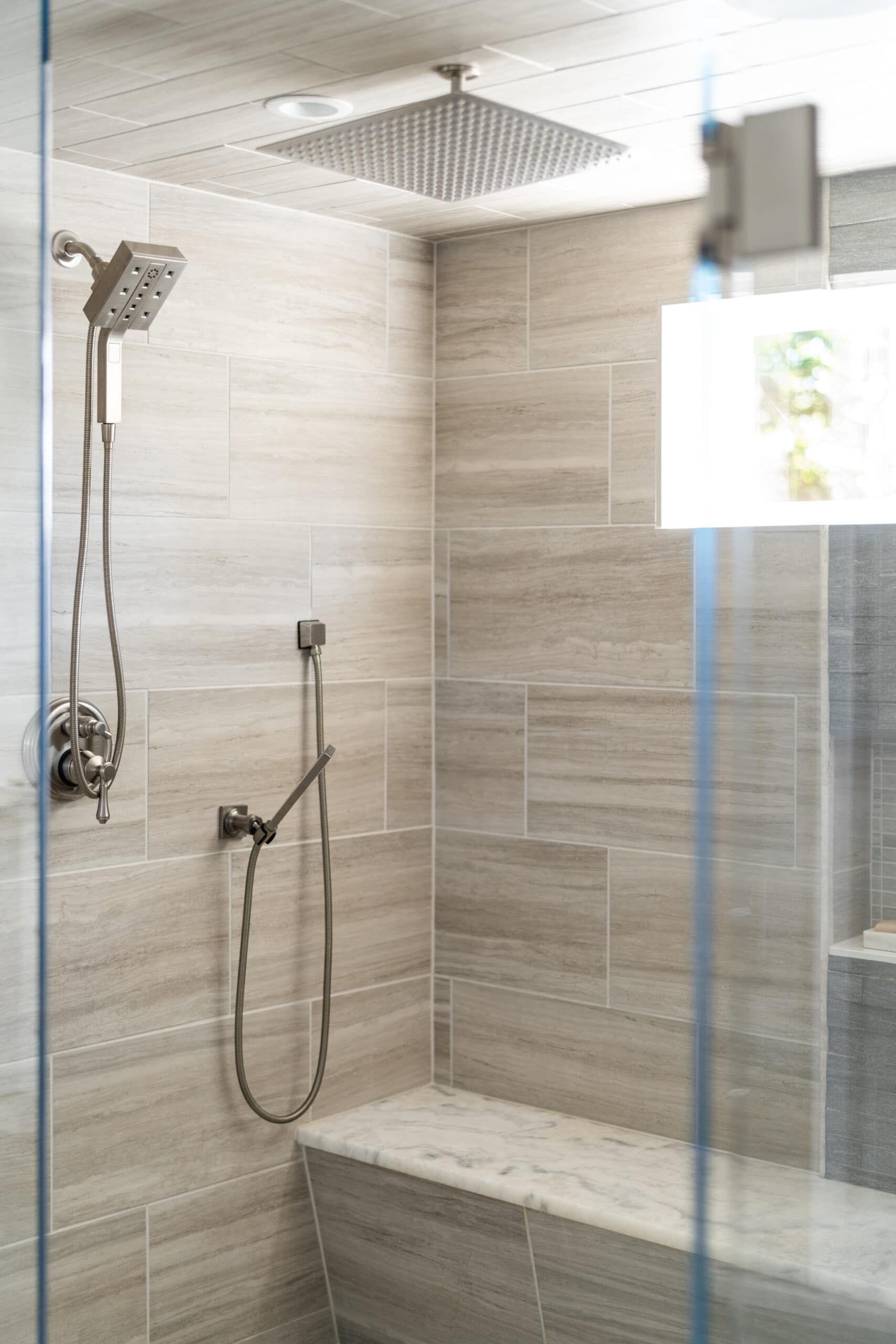 walk-in shower with with square shower head and integrated stone top bench as seen through its open, clear glass door