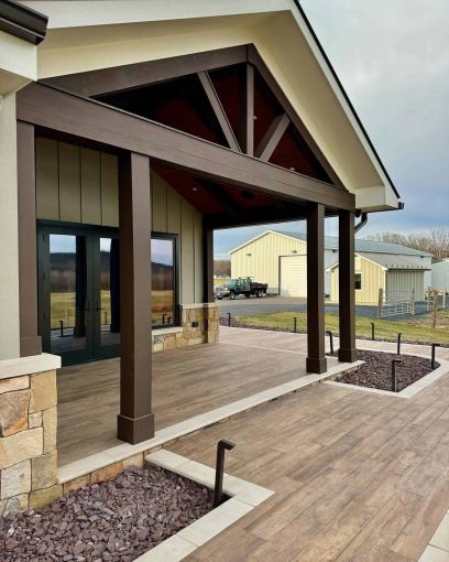a rustic patio with wooden walkways framed with stone, two large sheds are in the background