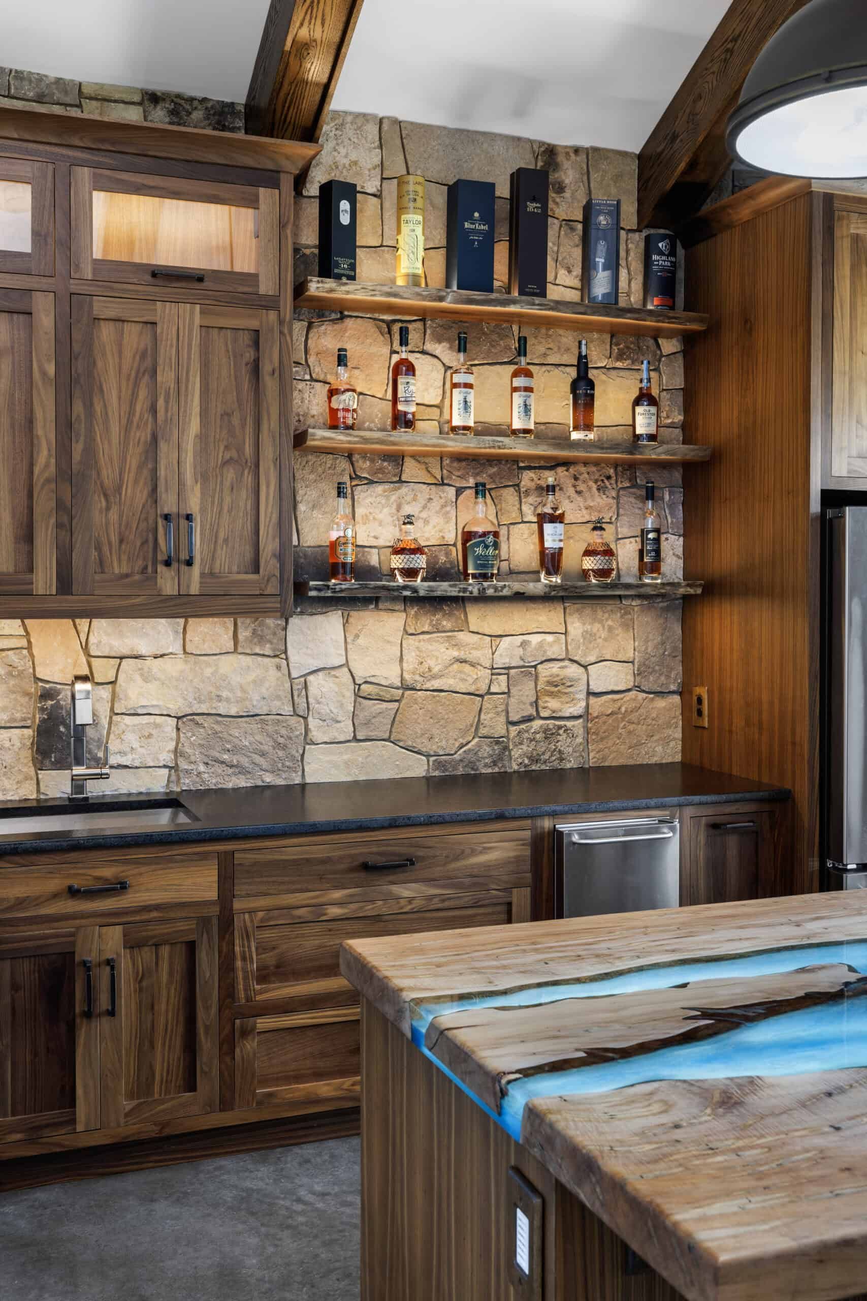 an in-home bar with natural stone walls and dark wood cabinets, a central wood island has an decorative effect evocative of bright flowing water