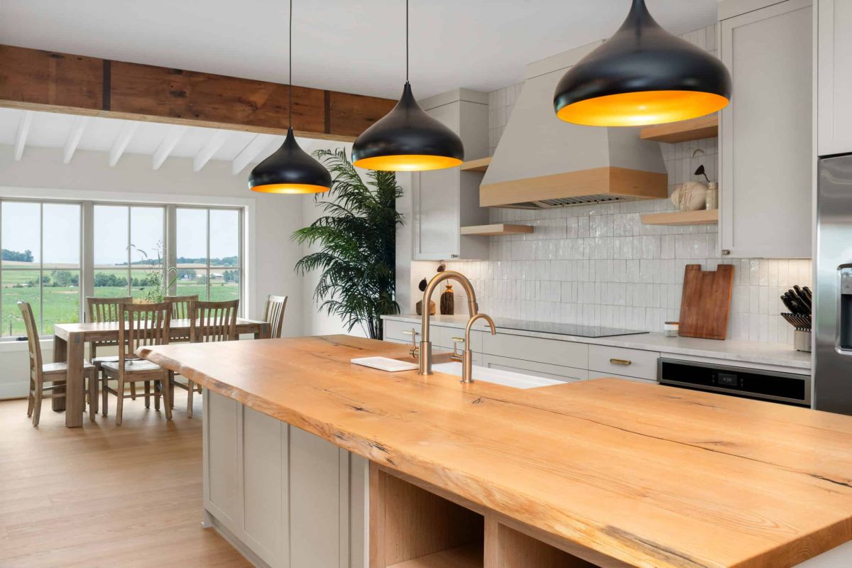 kitchen island with light brown wood surface, black hanging lamps, and sink with brass facuet