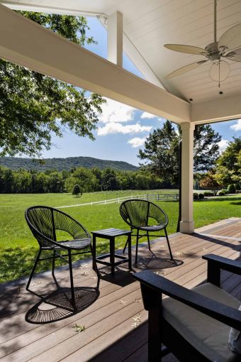 outdoor wooden porch, with three black chairs, overlooking green hills on a sunny day