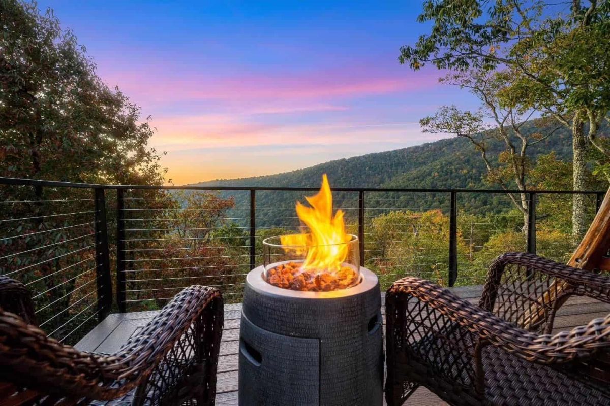 view of green hills at dusk as scene from a deck behind two wicker chairs and a fire