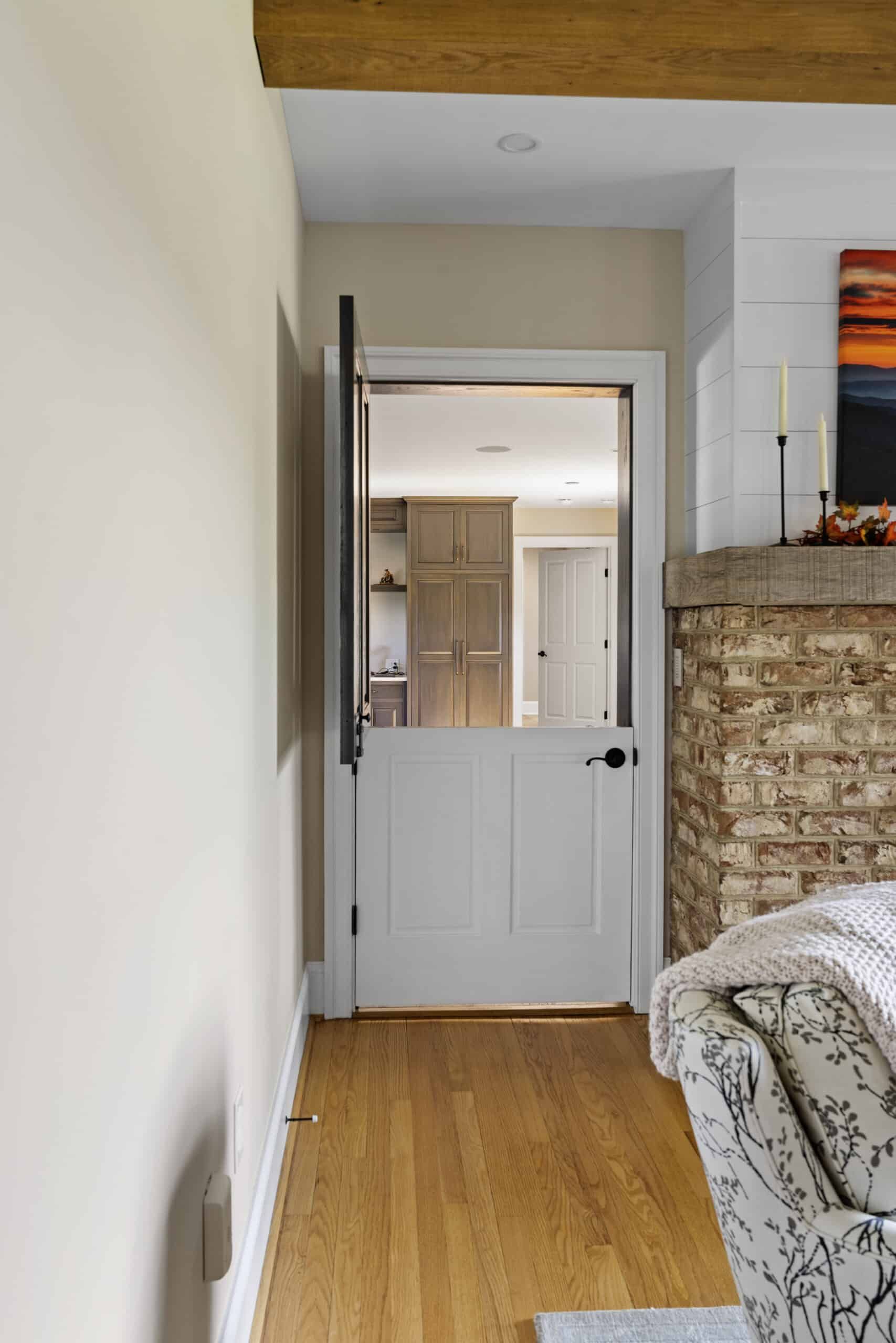Cropped view of a dutch door with the upper part open in a living room. To the door's right is what appears to be part of a brick fireplace