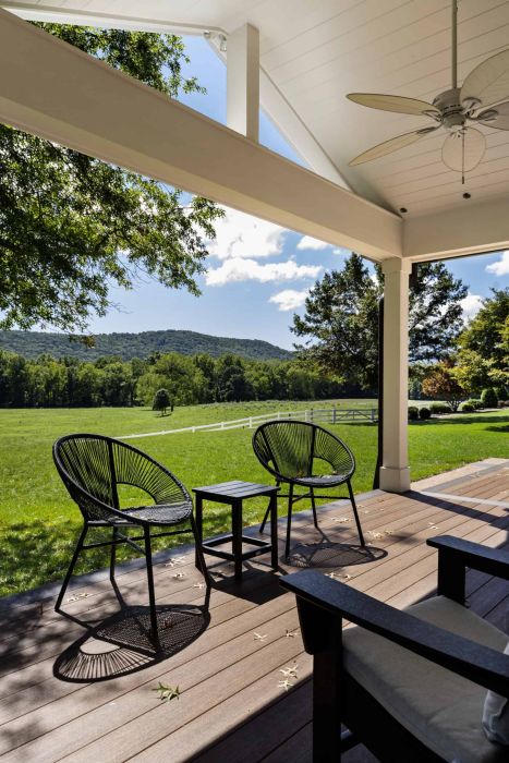 outdoor wooden porch, with three black chairs, overlooking green hills on a sunny day