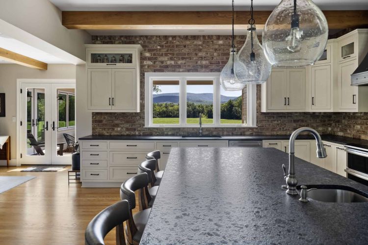 a kitchen island in a home with exposed brick walls, wood floors, white cabinets, and decorative light features