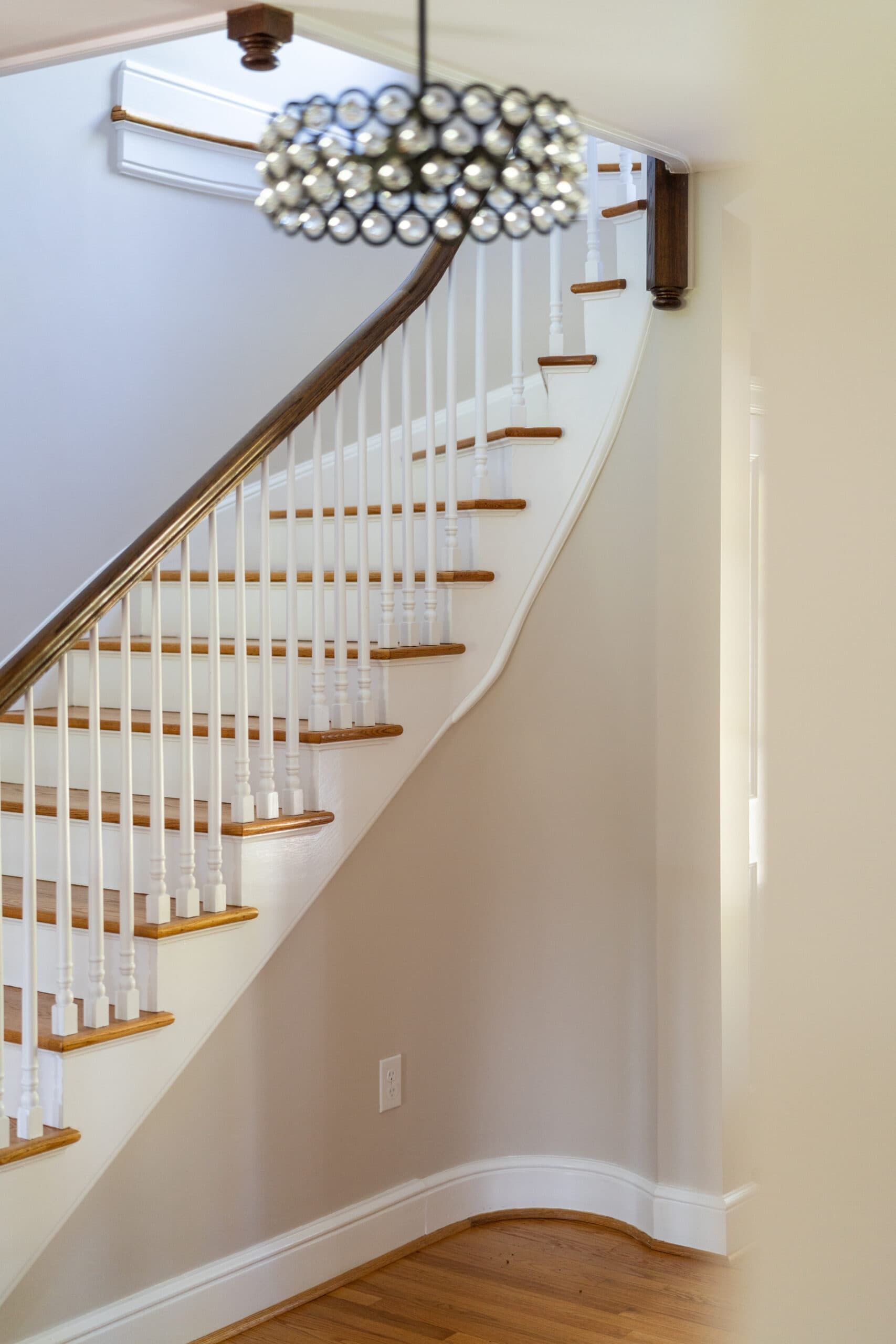 Close-up view of a white staircase with wood tread, white baluster, and wood guard rail. A vintage crystal hanging light fixture is present.