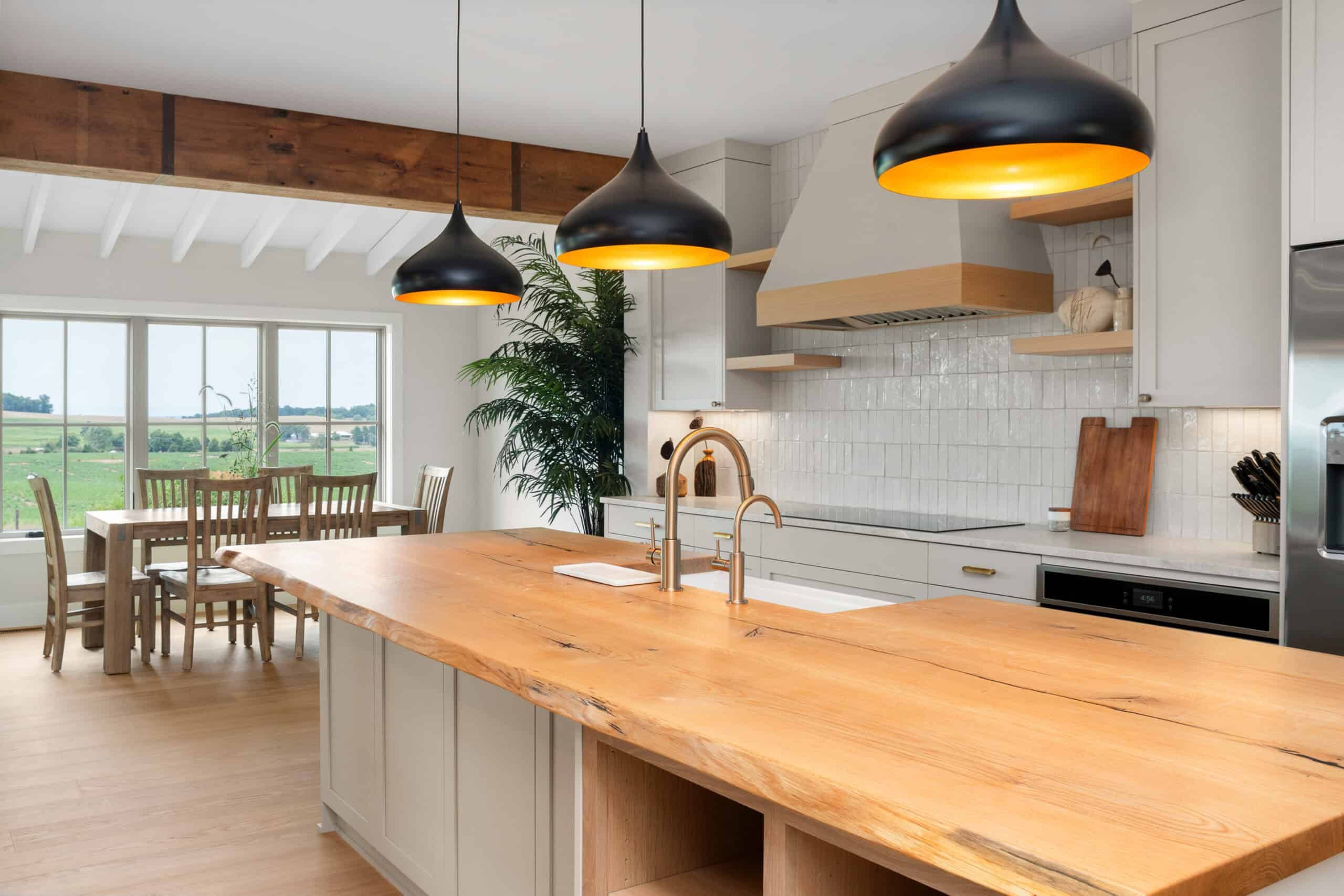kitchen island with light brown wood surface, black hanging lamps, and sink with brass facuet