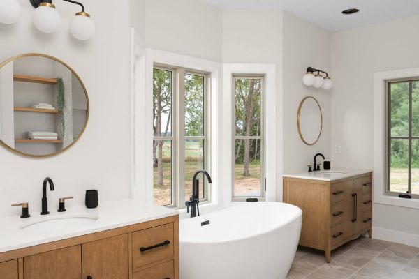 wide angle view of a bathroom with white walls and twin wood vanities with white tops. Between the vanities is a small white tub in front of five windows